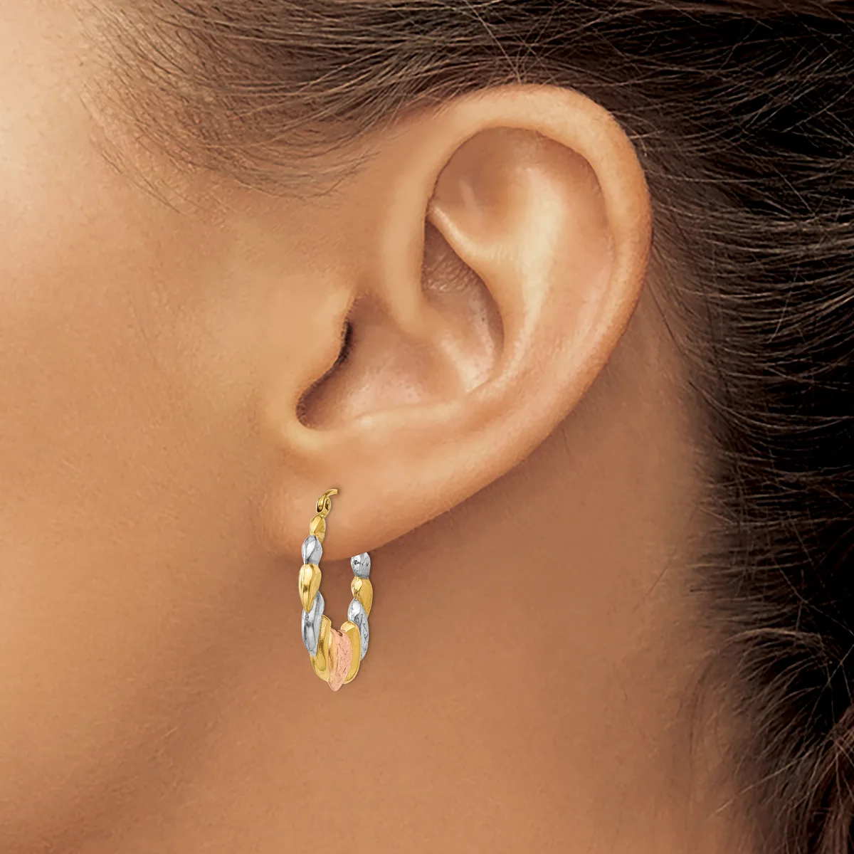 A person wearing gold and silver textured hoop earrings with small beads, shown from the side view of their ear and neck.