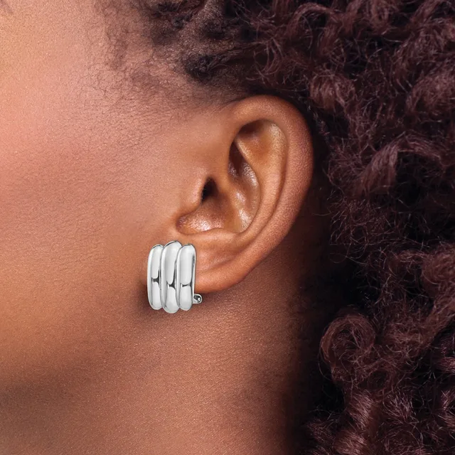 A person wearing a pair of chunky silver striped clip-on earrings on their earlobe, shown in profile view.