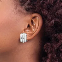 A person wearing a pair of chunky silver striped clip-on earrings on their earlobe, shown in profile view.