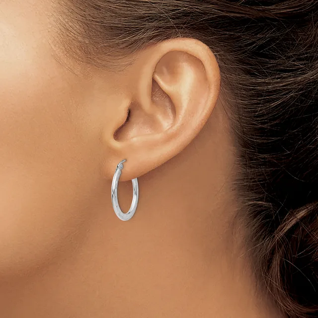 A person wearing a pair of polished silver hoop earrings, shown from the side profile of their ear and neck.