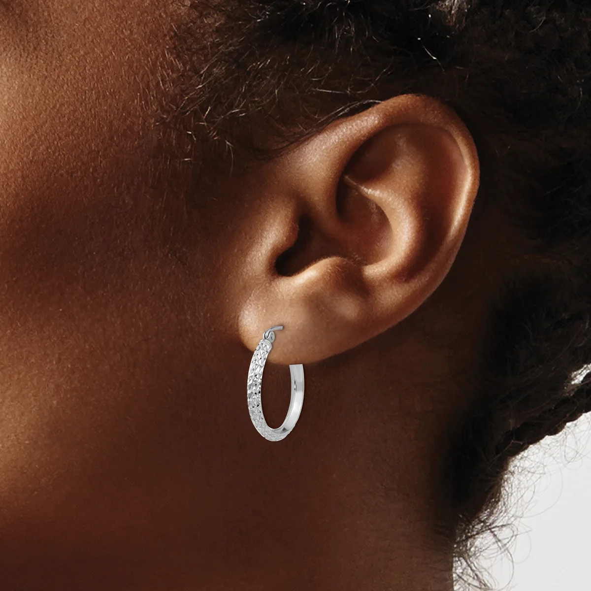 A person wearing a textured silver hoop earring in their pierced earlobe, shown in profile against their brown skin tone.