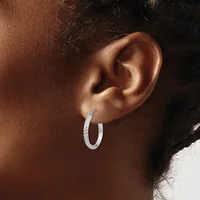 A person wearing a textured silver hoop earring in their pierced earlobe, shown in profile against their brown skin tone.