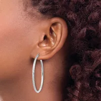 A person wearing large oval hoop earrings with a textured surface, shown in profile against dark curly hair.
