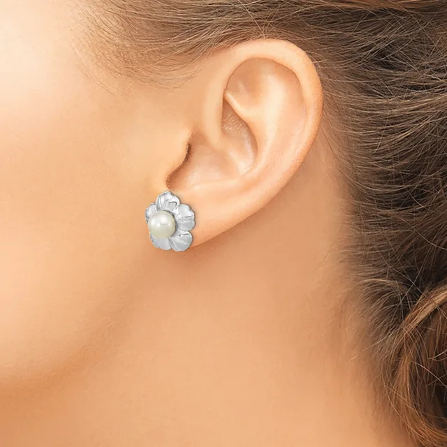 A woman wearing a silver flower-shaped stud earring with a white pearl center, shown on her earlobe.