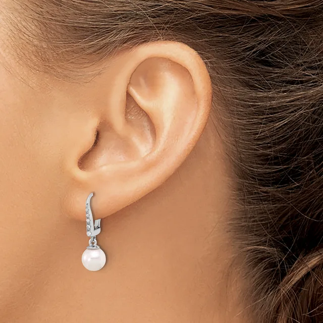 A woman wears a silver drop earring with a white pearl and diamond accents on her left ear.