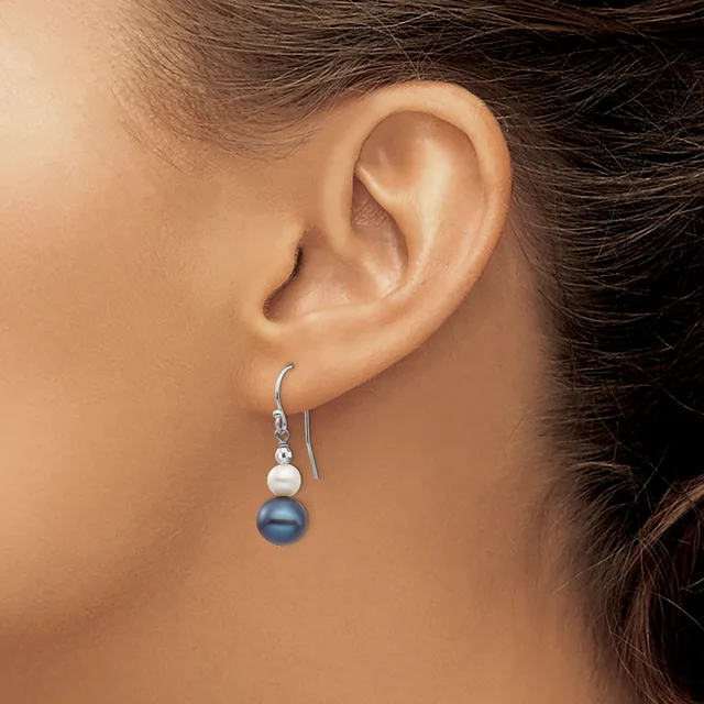 A person wearing silver hook earrings with a white pearl and blue pearl suspended below, shown from the side view of their ear.