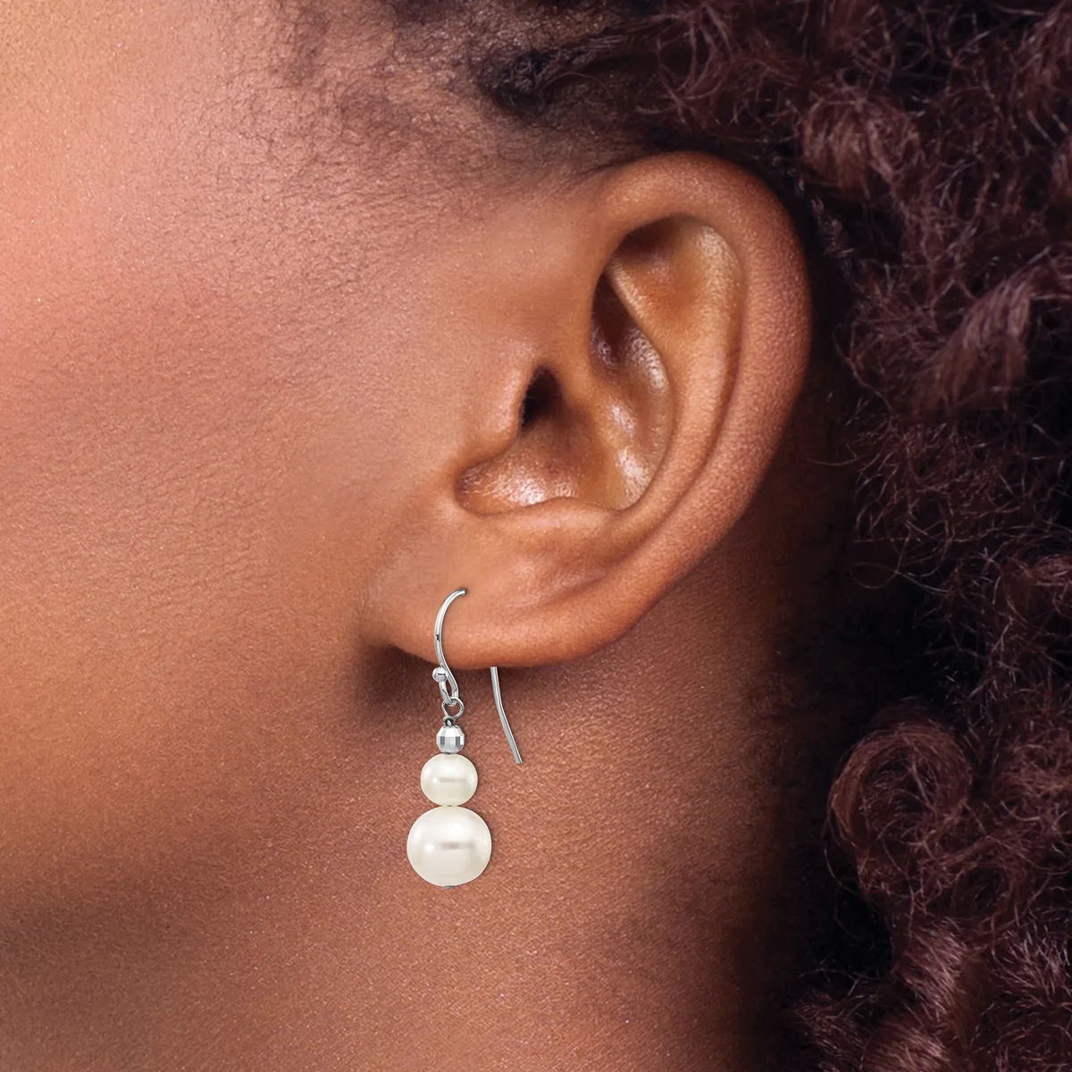 A person wearing silver hook earrings with two stacked white pearl drops on each ear.