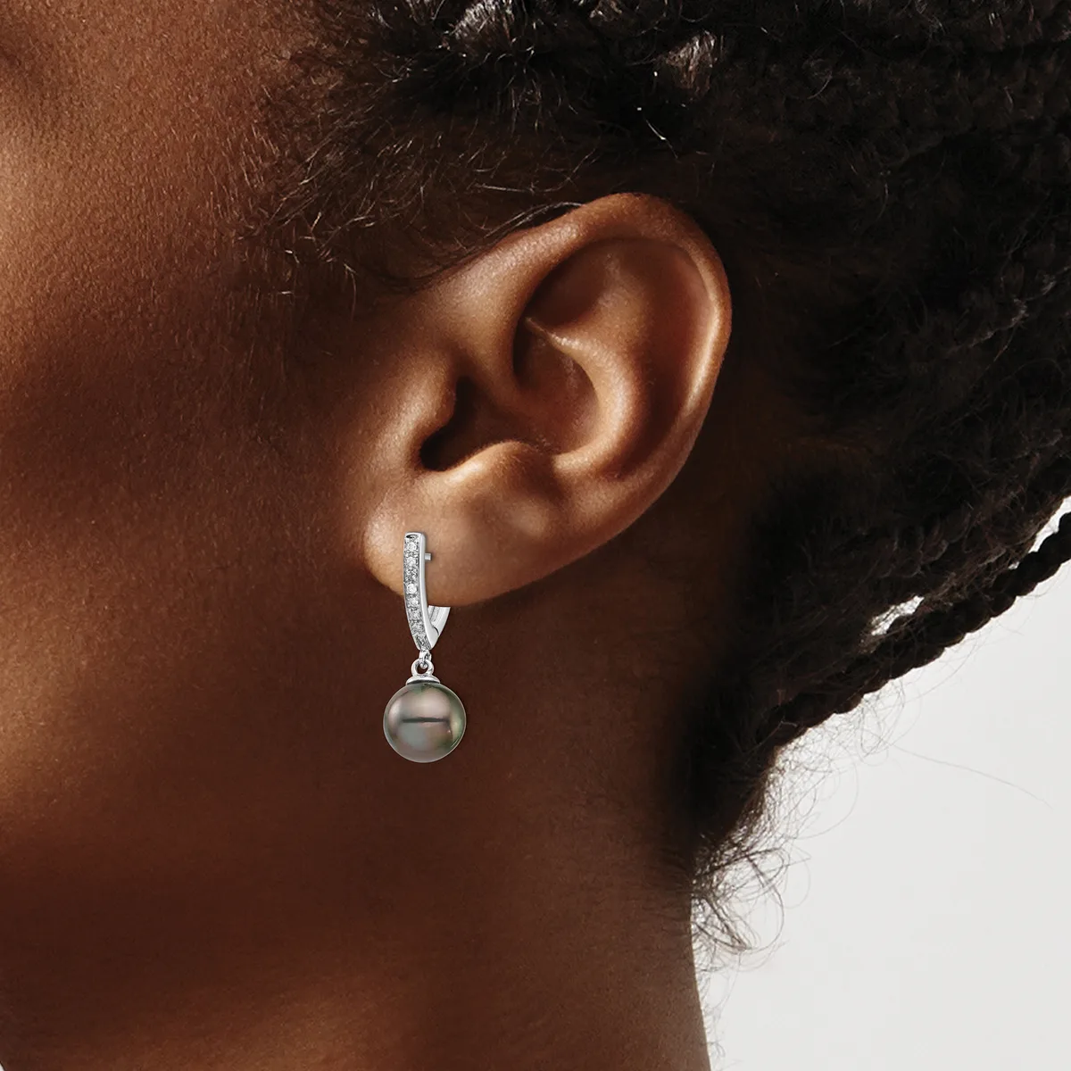 A person wearing a dangling earring with a silver hook, diamond accents, and a gray pearl drop, shown from the side against a neutral background.