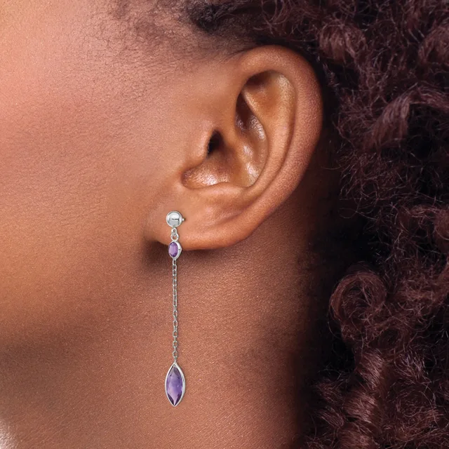 A person wearing a long dangling earring with a small round stone at the top connected by a delicate chain to an elongated purple stone at the bottom.