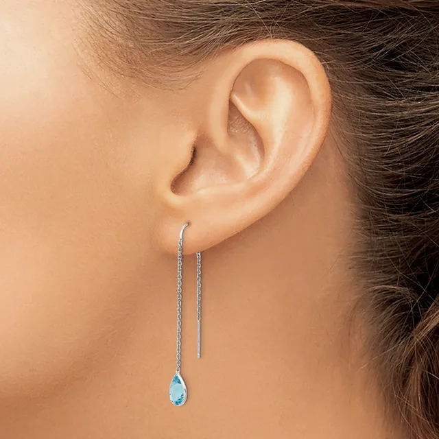 A woman wearing long threader earrings with small blue teardrop gemstones hanging from thin silver chains.