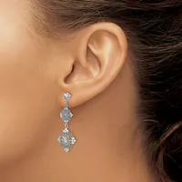 A woman wearing a long dangling earring with two diamond-shaped clusters connected by a thin chain, displayed against her ear.