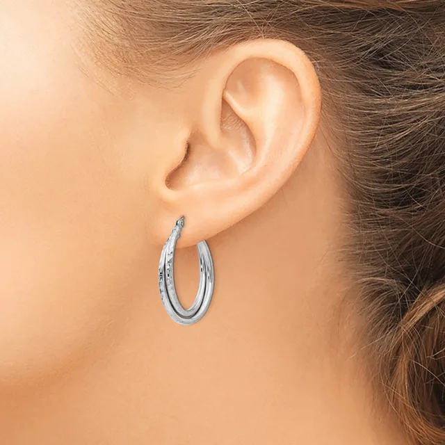 A woman wearing a pair of polished silver hoop earrings with a textured surface, shown from the side view near her ear.