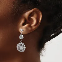 A woman wearing silver-toned drop earrings with small round stones at the top and larger ornate flower-shaped pendants below, shown from the side profile of her ear and neck.