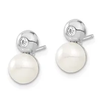 A pair of silver drop earrings with round white pearls suspended below small circular bezels set with clear round stones.