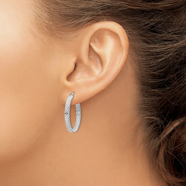 A person wearing textured silver hoop earrings, shown from the side profile with their ear and part of their face and brown hair visible.