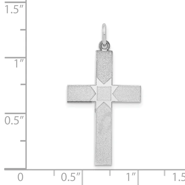 A silver cross pendant with a textured matte finish and a small square detail at the center, shown against a measurement scale indicating its size is approximately one inch wide and one and a quarter inches tall.