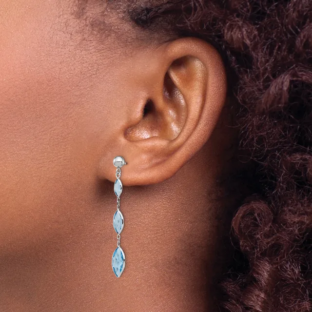 A person wearing a long dangle earring with marquise-shaped stones set in silver metal, shown from the side profile against their neck and shoulder.