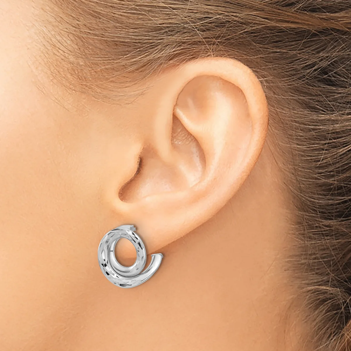 A silver textured chunky hoop earring worn on a person's earlobe, shown from the side view.