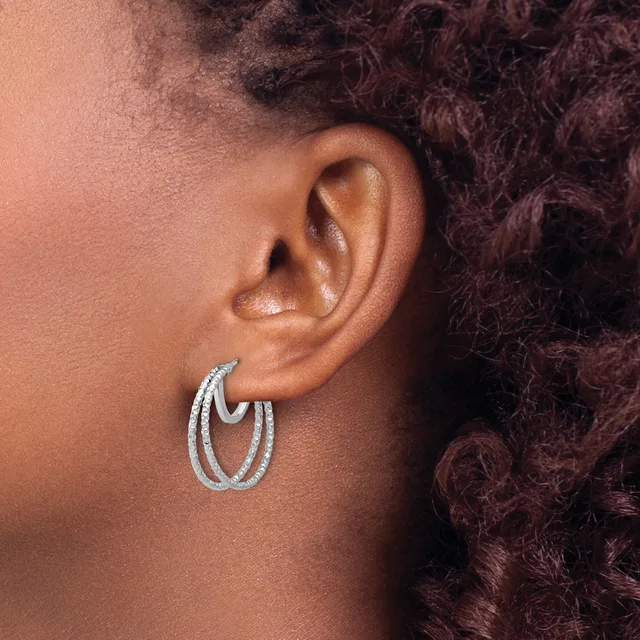 A person wearing textured silver-toned double hoop earrings, shown in profile from the side of their face and ear.