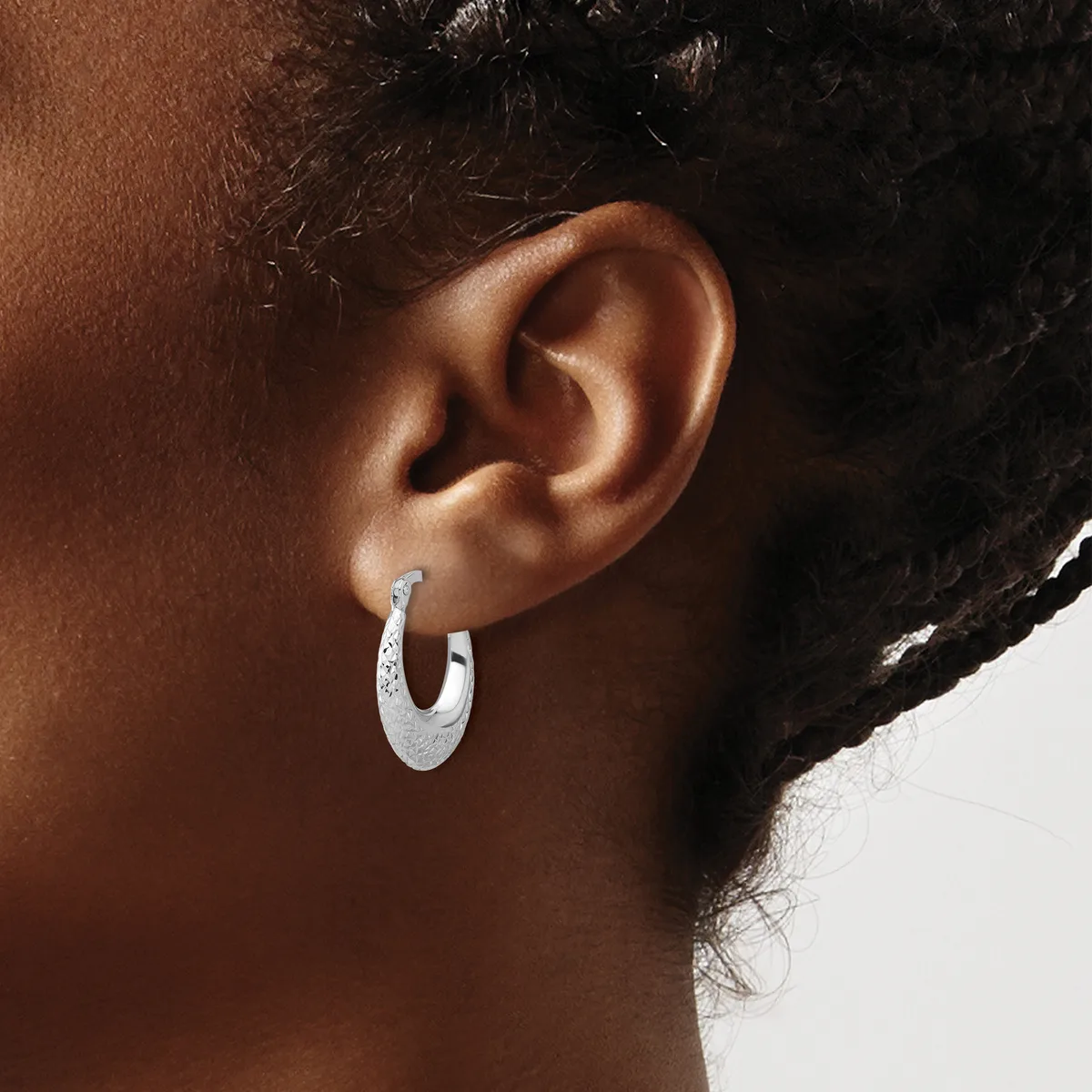A person wearing a textured silver hoop earring in their earlobe, shown in profile against a white background.