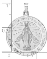 Silver religious medal pendant featuring the Virgin Mary with outstretched arms and radiating rays, surrounded by circular text, shown against a measurement scale.