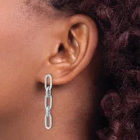 A silver chain link earring hangs from a pierced earlobe on a person with medium skin tone and dark curly hair.