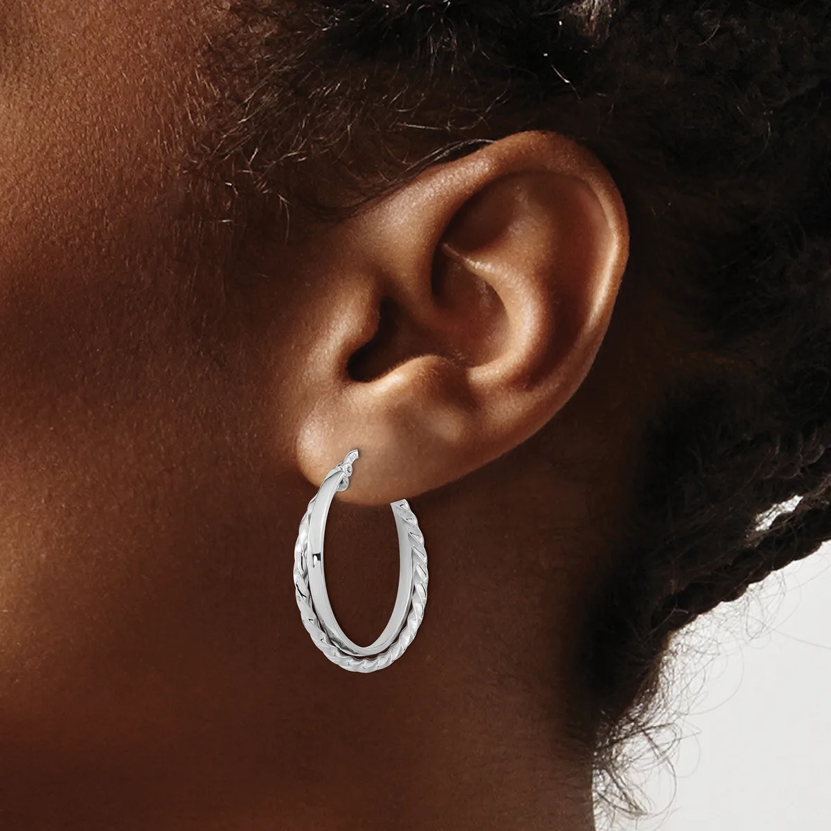 A person wearing textured silver hoop earrings, shown in profile from the side of their face and ear against a brown and white background.