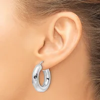 A polished silver hoop earring with a textured surface worn on a model's ear.