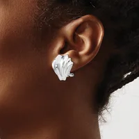 A white sculptural earring shaped like an abstract shell or fan is worn on the earlobe of a person with brown skin and dark hair.