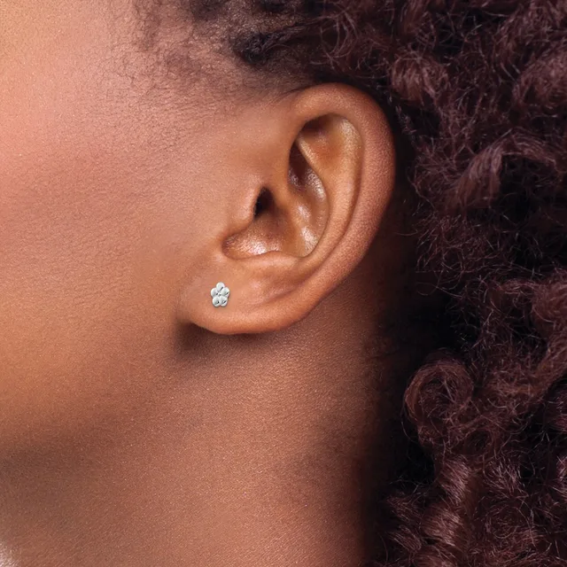 A person with dark curly hair wears a small silver stud earring with a oval stone in their pierced earlobe, shown in profile against their neck and shoulder.
