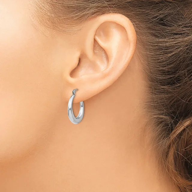 A woman wearing a pair of polished silver hoop earrings, shown from the side profile with her ear and part of her face visible.
