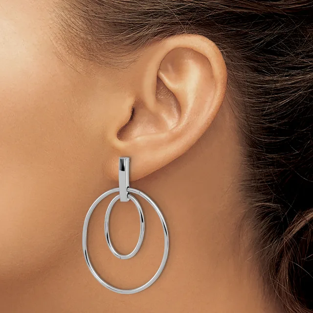 A woman wearing a pair of silver-toned double oval hoop earrings hanging from her earlobes.