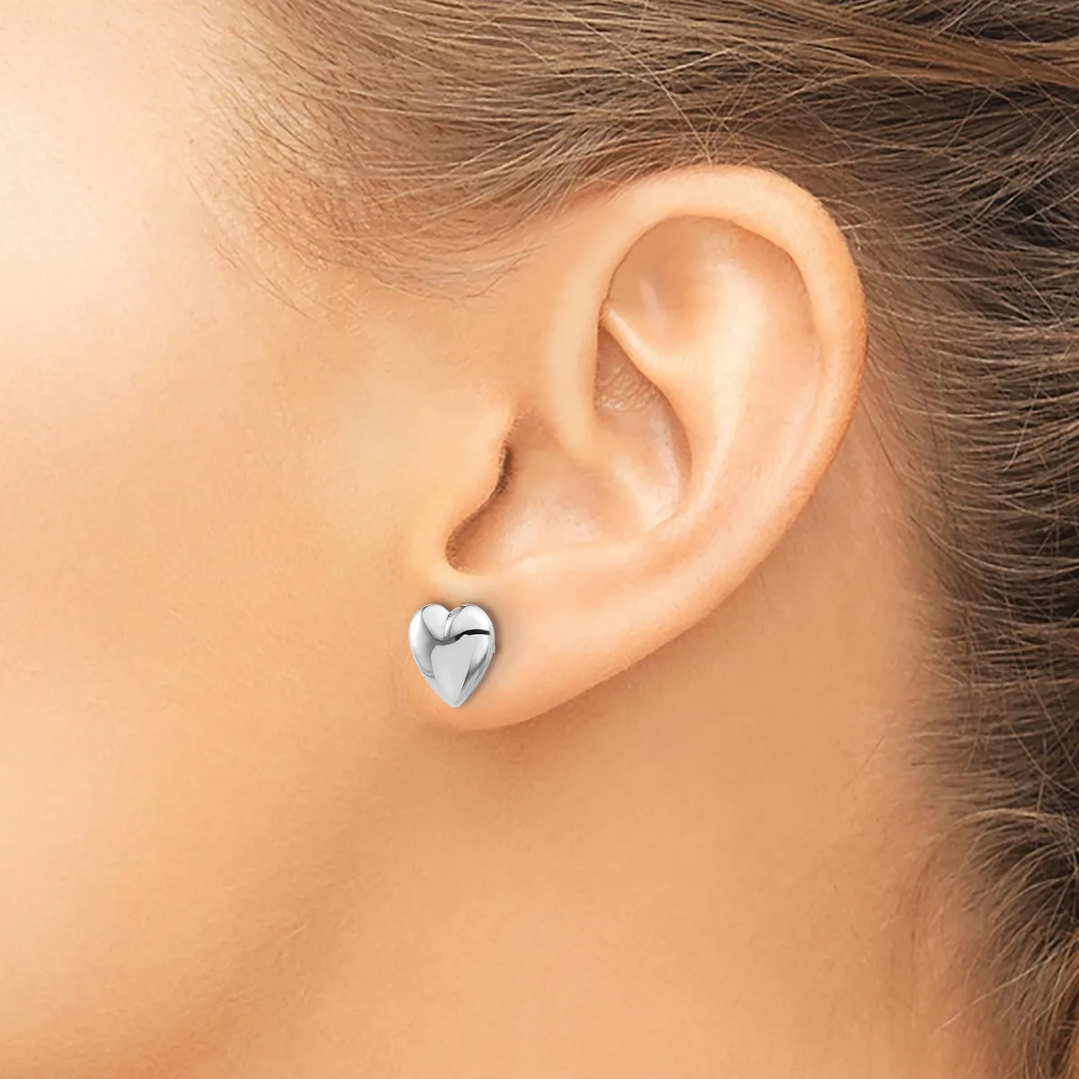 A polished silver heart-shaped stud earring worn on a person's earlobe.