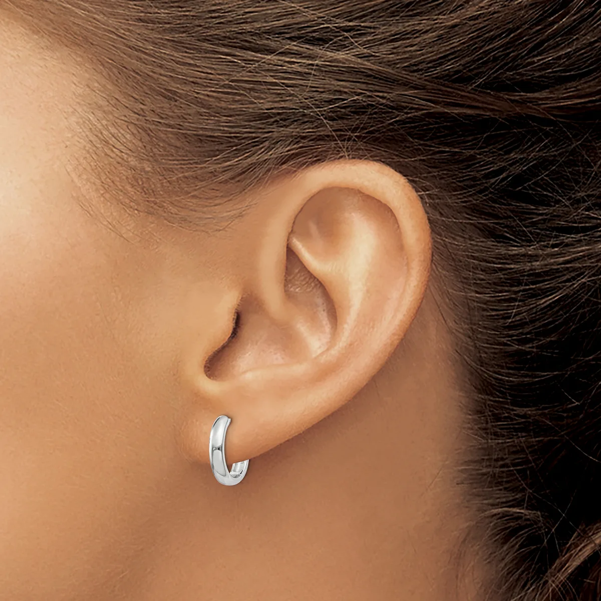 A person wearing a polished silver hoop earring with a grooved texture, shown from the side view of their ear.