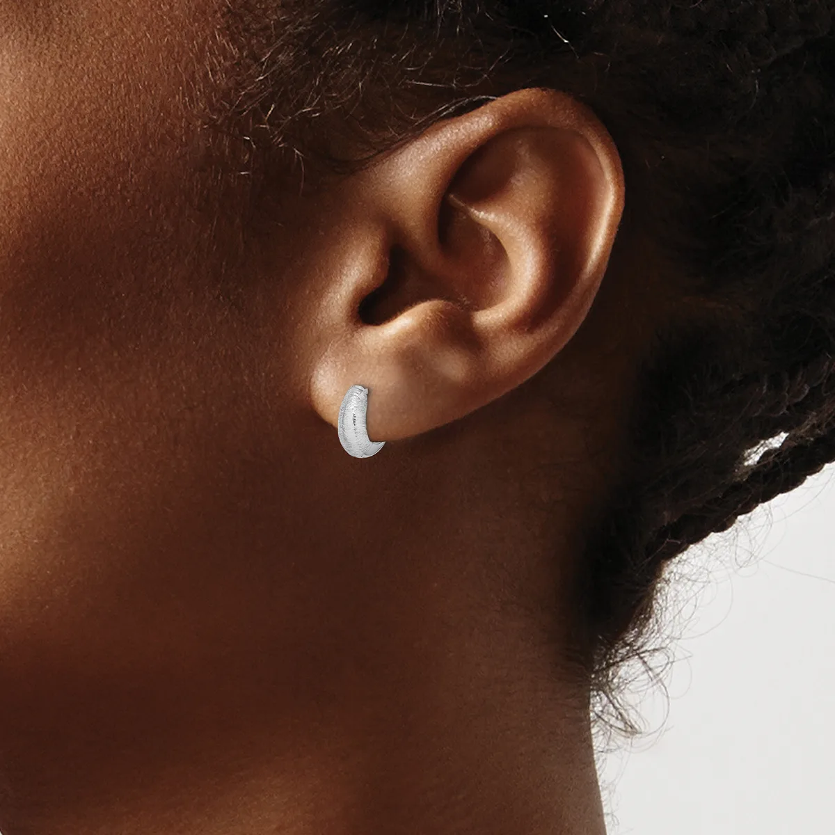 A person wearing a small curved silver crescent-shaped earring in their earlobe, shown in profile against a neutral background.