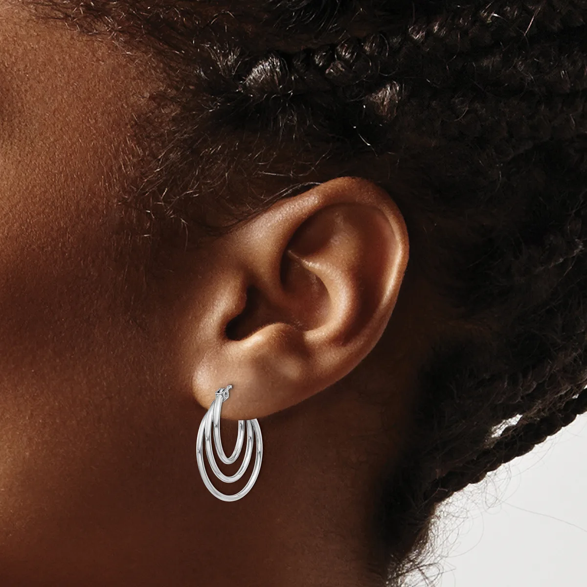 A person wearing triple-loop silver hoop earrings, shown from the side profile with their ear and dark hair visible against a neutral background.