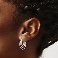 A person wearing triple-loop silver hoop earrings, shown from the side profile with their ear and dark hair visible against a neutral background.
