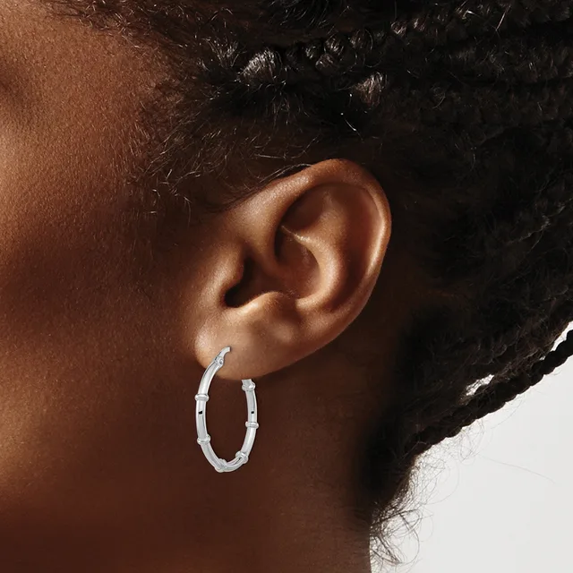A person wearing a pair of silver textured oval hoop earrings, shown from a side profile view of their ear and neck.