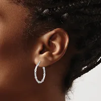 A person wearing a pair of silver textured oval hoop earrings, shown from a side profile view of their ear and neck.