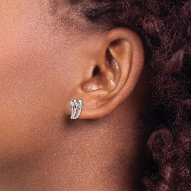 A person wearing small silver hoop earrings with a grooved or ridged texture on their earlobe, shown in profile.