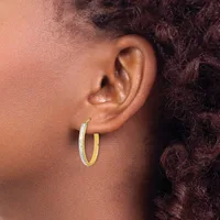 A person wearing two-toned gold hoop earrings with a textured finish, shown in profile view against their ear.