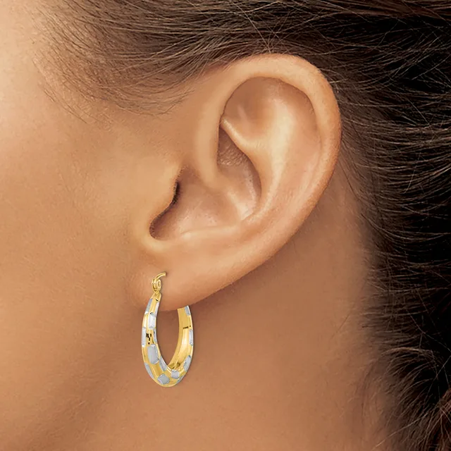 A person wearing a pair of two-toned gold hoop earrings with a textured surface, shown from the side profile of their ear.