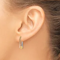 A person wearing two-tone rectangular hoop earrings with a textured surface, shown from the side view of their ear.
