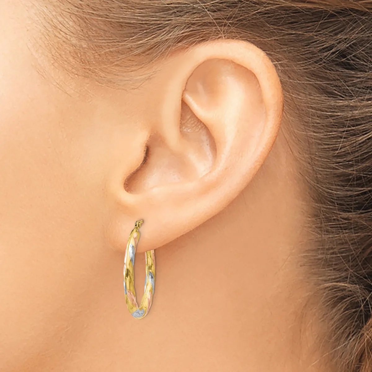 A person wearing two-tone gold hoop earrings with a textured surface, shown from the side view against their ear.
