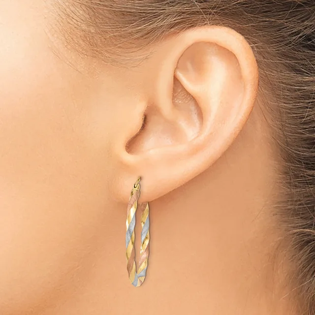 A woman's ear wearing a pair of twisted oval hoop earrings in two-tone gold and silver metal.