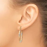 A woman's ear wearing a pair of twisted oval hoop earrings in two-tone gold and silver metal.