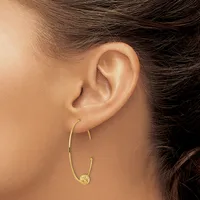 A person wearing gold hoop earrings with a small textured disc charm hanging from one ear, shown in profile against a neutral background.