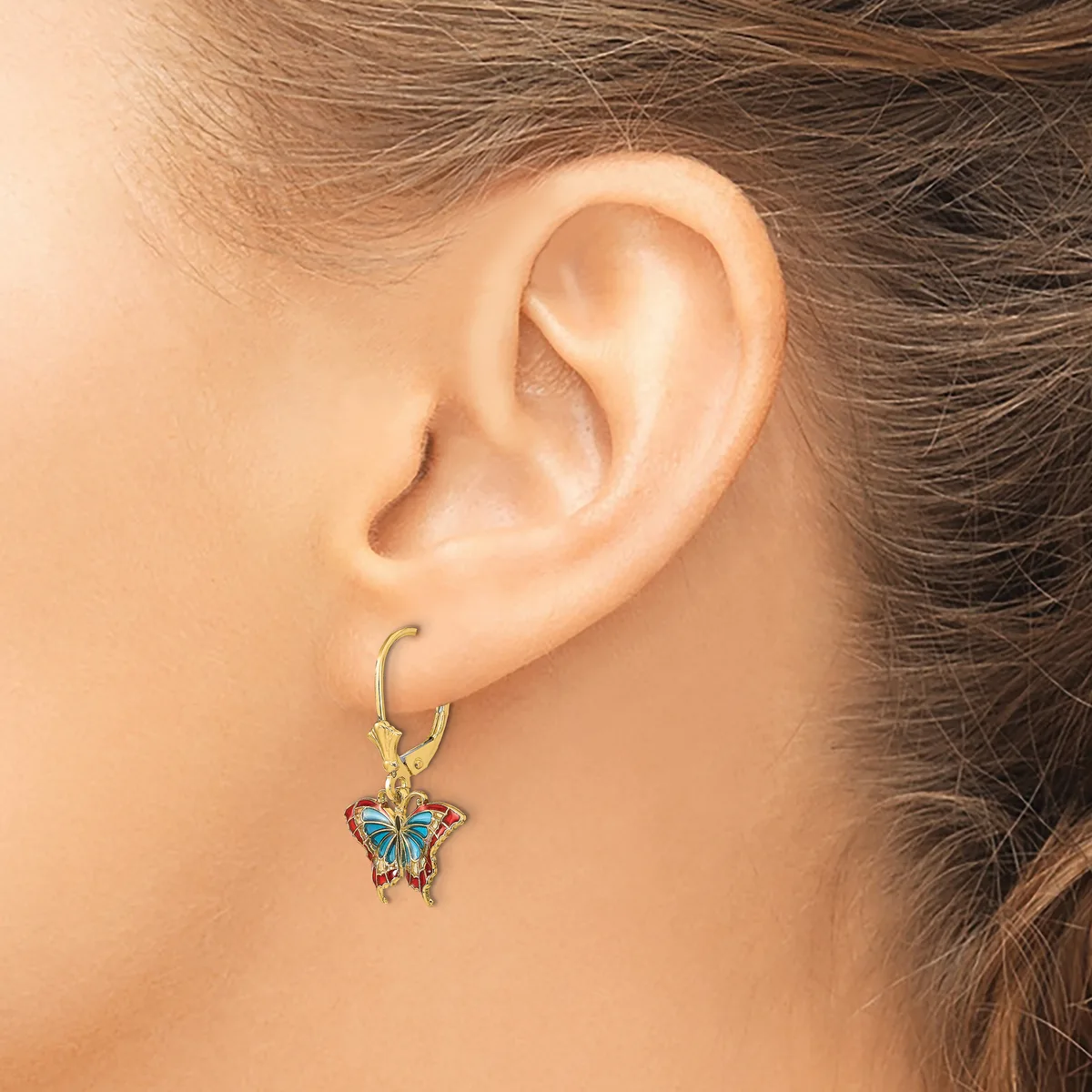 A woman wearing a gold hoop earring with a small blue and copper butterfly pendant charm hanging from it.