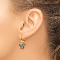 A woman wearing a gold hoop earring with a small blue and copper butterfly pendant charm hanging from it.