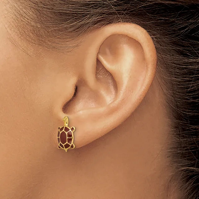A gold turtle-shaped earring with a red enamel shell is worn on a pierced earlobe.